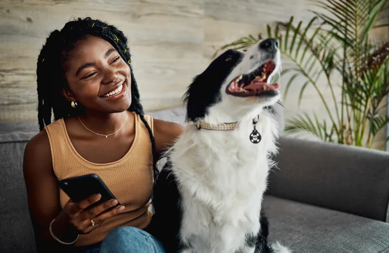 Woman smiling at her phone beside her dog, who wears a DocuPet tag